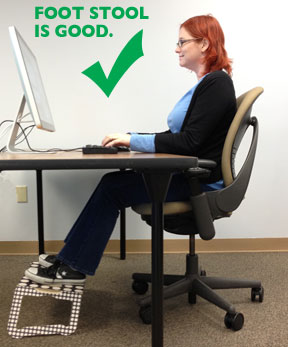 Woman working on computer at desk with foot stool, feet are flat on the stool and posture is straight